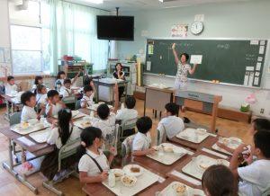 子供達がご飯を食べながら、手を挙げて、クイズを参加している写真