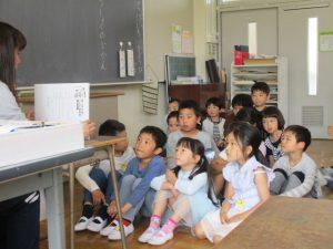 子供達が地面に座って、先生の話を聞いている写真