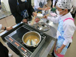 調味料を煮立たせた鍋にサバを入れる生徒との写真