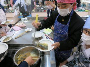 煮立った鍋から魚を慎重に取り出す生徒の写真