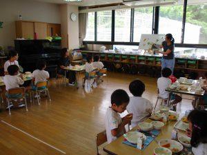 子供達は給食を食べながら、先生の話を聞いている写真
