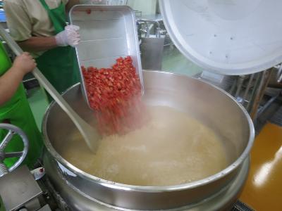 大きなみそ汁の釜にトマトを入れる調理員さん