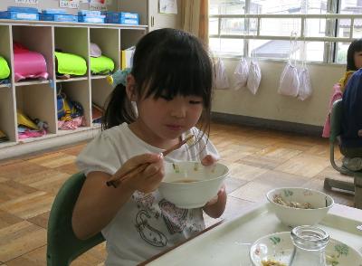 お碗を持ち、おはしで豆腐をつまむ小学1年生