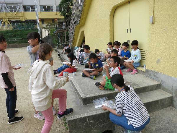 運動場で一緒に弁当給食を食べている低学年と高学年