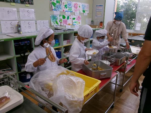 担任の先生に教えてもらいながら配膳をする1年生