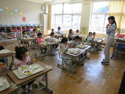 初めての学校給食を食べながら先生のお話を聞く小学1年生