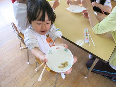 箸でつまんだ豆を誇らしげに見せてくれる幼稚園児