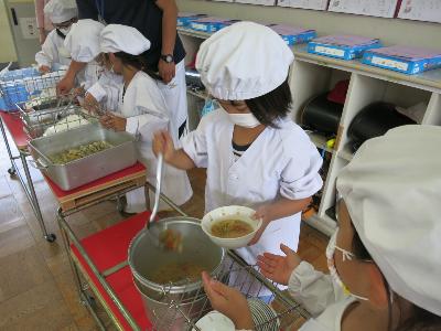 トマトと玉ねぎのみそ汁をよそう小学1年生