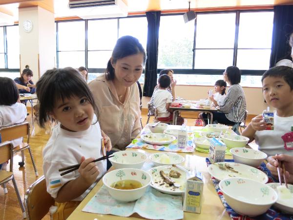 お母さんに見守られながら魚を食べる園児