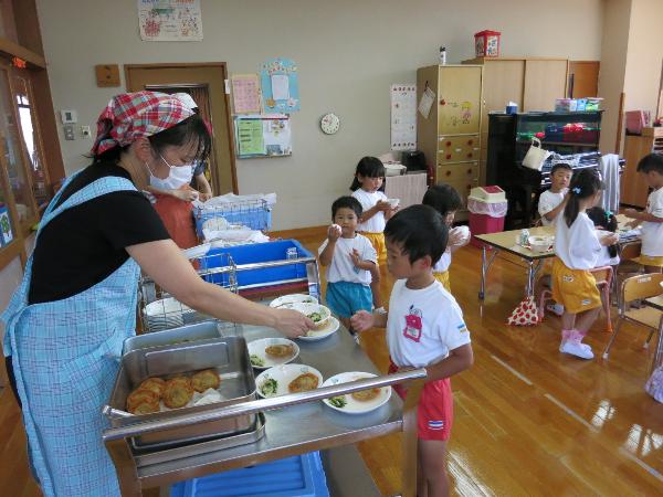 順番に給食をもらいに行く幼稚園児