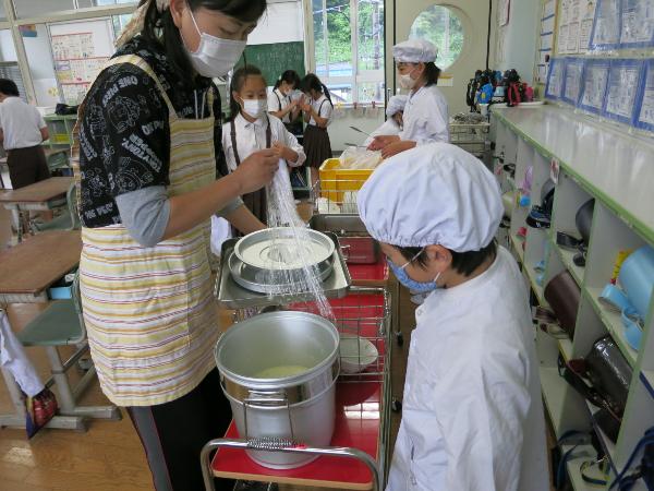 食缶を開けて確認する給食当番と担任の先生