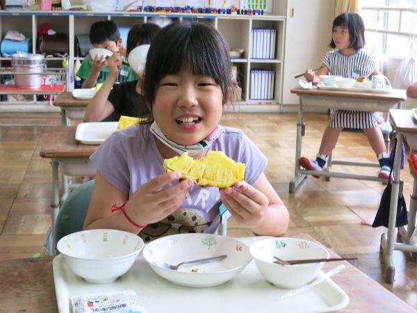 おいしそうにパイナップルを食べる児童