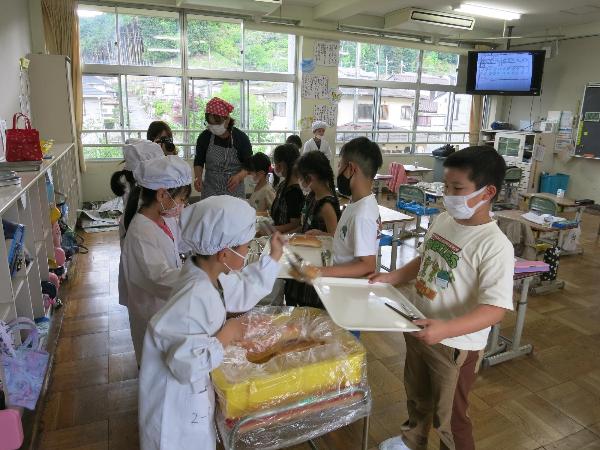 新聞社の取材カメラを向けられながら配膳をする千早小吹台小学校2年生