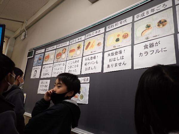 給食の歴史の掲示物を見に集まる千早小吹台小学校4年生