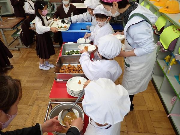 先生方に手伝ってもらいながら配膳をがんばる赤阪小学校1年生