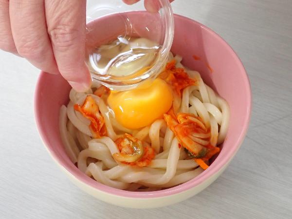 熱いうどんに生卵をのせるところ
